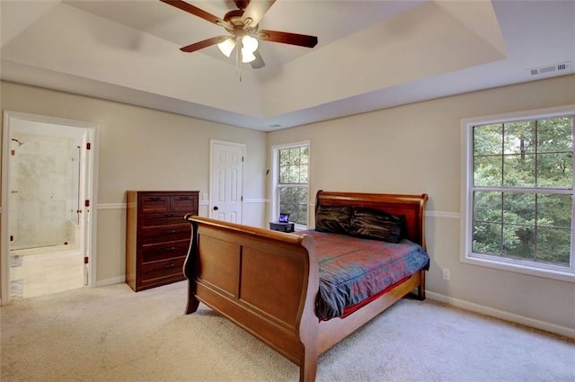 bedroom with multiple windows, a tray ceiling, ensuite bath, and light colored carpet