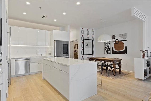 kitchen with a kitchen island, a sink, stainless steel appliances, white cabinetry, and light wood-type flooring