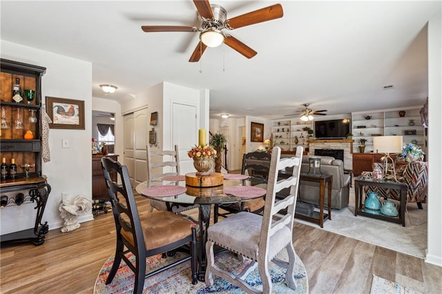 dining area featuring visible vents, ceiling fan, a fireplace, and light wood-style flooring