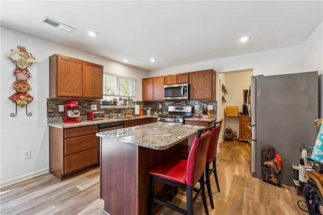 kitchen with light stone counters, a kitchen island, visible vents, a kitchen breakfast bar, and appliances with stainless steel finishes