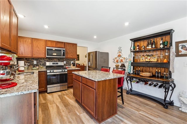 kitchen with appliances with stainless steel finishes, brown cabinets, a center island, light wood-style floors, and a sink