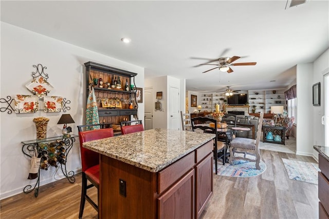 kitchen with a center island, a fireplace, light wood-style floors, open floor plan, and ceiling fan