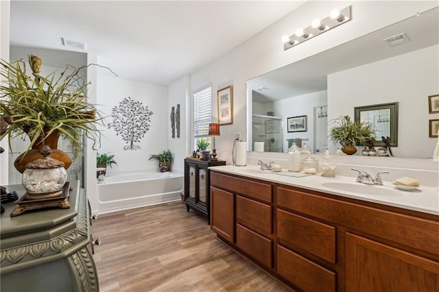 bathroom with a sink, wood finished floors, a garden tub, and visible vents