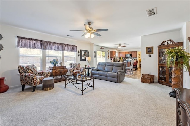 living room with light carpet, ceiling fan, visible vents, and baseboards