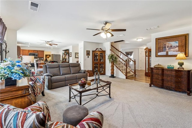 living area featuring light carpet, visible vents, ceiling fan, and stairway