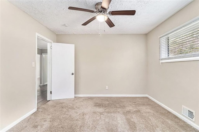 carpeted empty room featuring a textured ceiling, ceiling fan, visible vents, and baseboards