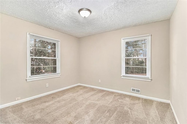 empty room featuring carpet, visible vents, a textured ceiling, and baseboards