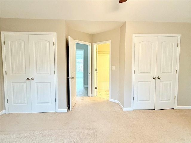 unfurnished bedroom with light carpet, two closets, and ceiling fan