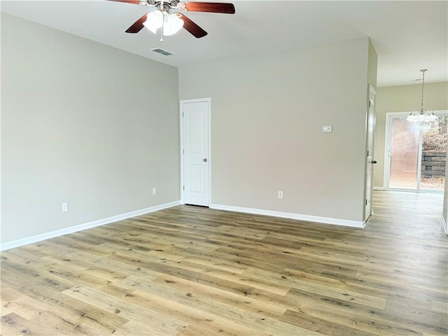 empty room with hardwood / wood-style floors and ceiling fan with notable chandelier