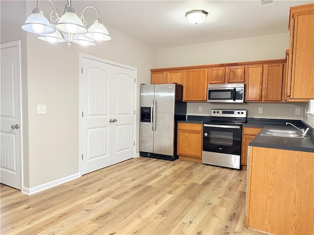 kitchen featuring sink, hanging light fixtures, light wood-type flooring, appliances with stainless steel finishes, and a notable chandelier