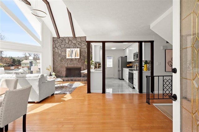 interior space with light wood-type flooring, high vaulted ceiling, beamed ceiling, and a stone fireplace