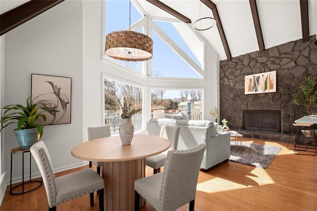 dining area featuring a fireplace, high vaulted ceiling, wood finished floors, and beamed ceiling