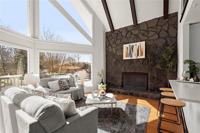 living room with high vaulted ceiling, beamed ceiling, a stone fireplace, and wood finished floors