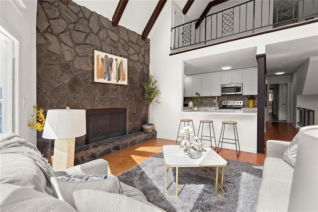 living room featuring high vaulted ceiling, a stone fireplace, beamed ceiling, and wood finished floors