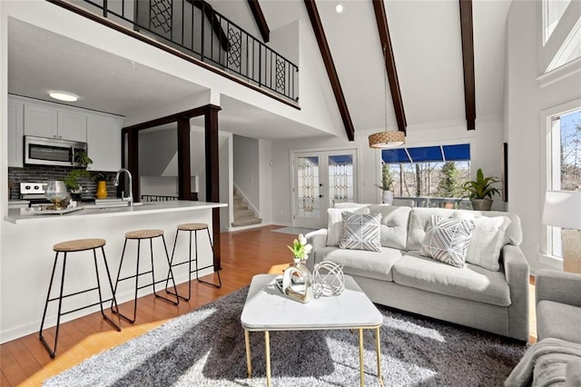 living area featuring high vaulted ceiling, french doors, stairway, and wood finished floors