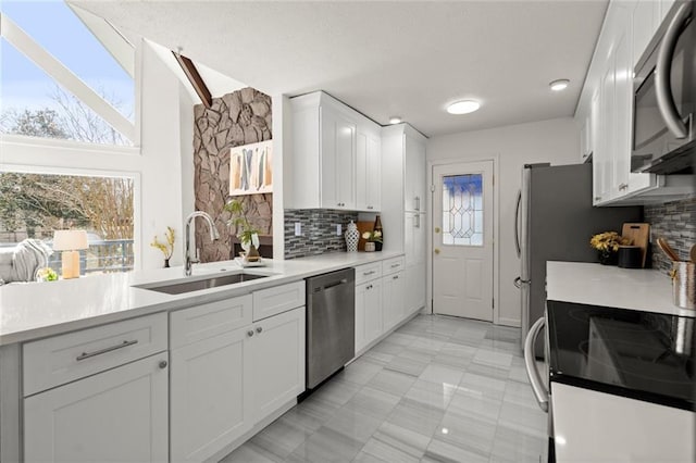 kitchen with tasteful backsplash, light countertops, appliances with stainless steel finishes, white cabinetry, and a sink