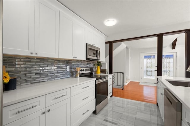 kitchen with white cabinets, decorative backsplash, stainless steel appliances, light countertops, and a sink