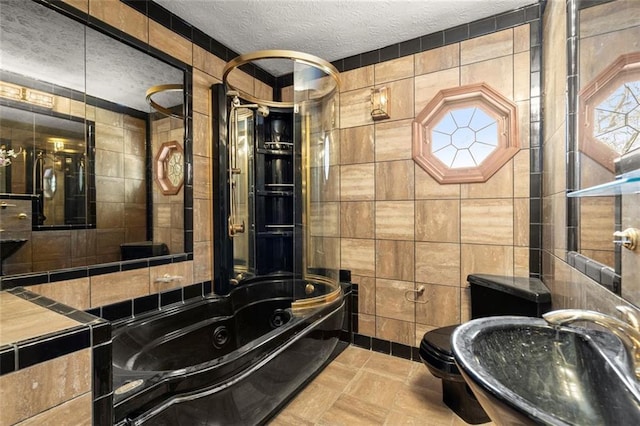 bathroom featuring a textured ceiling, toilet, a sink, tile walls, and a tub with jets