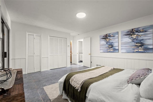 tiled bedroom featuring wainscoting and two closets