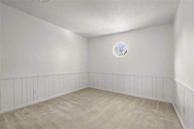 carpeted spare room with a textured ceiling and wainscoting