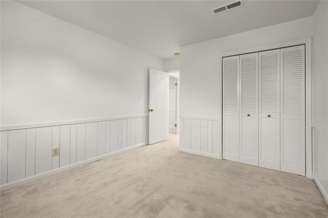 unfurnished bedroom featuring carpet floors, visible vents, a closet, and wainscoting