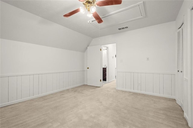 additional living space featuring visible vents, lofted ceiling, a wainscoted wall, ceiling fan, and carpet