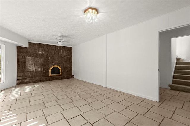 unfurnished living room with a large fireplace, baseboards, ceiling fan, stairs, and a textured ceiling