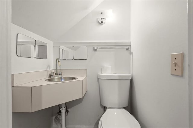 half bathroom featuring toilet, vaulted ceiling, and a sink