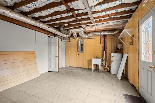 basement featuring wood walls, a sink, water heater, electric panel, and plenty of natural light