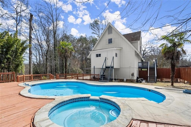 view of swimming pool with a pool with connected hot tub, stairs, fence, and a wooden deck