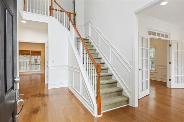 stairway with wood-type flooring, a towering ceiling, and crown molding