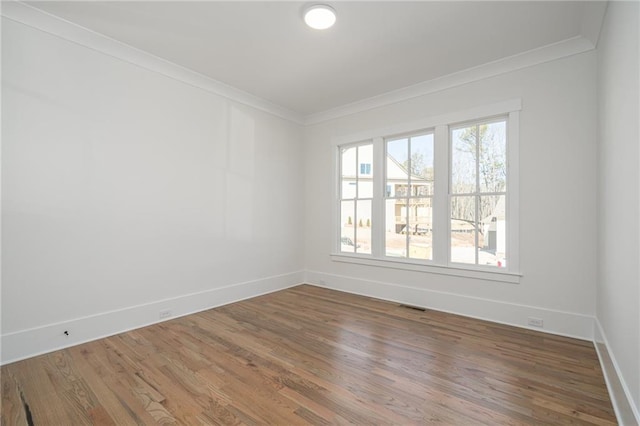 empty room with visible vents, crown molding, baseboards, and wood finished floors