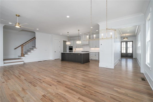 kitchen with visible vents, open floor plan, light countertops, crown molding, and light wood-type flooring