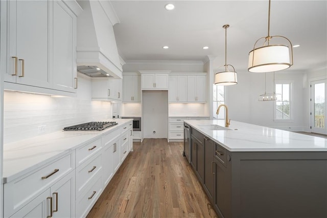 kitchen with premium range hood, a sink, white cabinets, backsplash, and crown molding