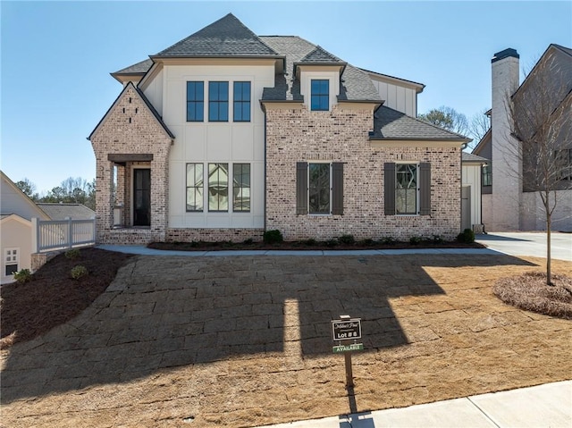 view of front facade featuring brick siding, fence, roof with shingles, stucco siding, and board and batten siding