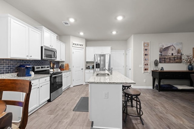 2046 Westbrook Rd, Commerce, GA 30530 - kitchen featuring appliances with stainless steel finishes, a sink, light wood finished floors, a kitchen bar, and backsplash