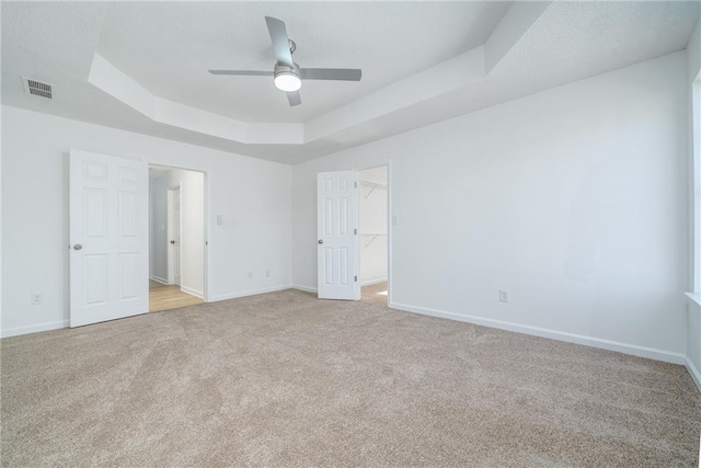 unfurnished bedroom featuring ceiling fan, a tray ceiling, a spacious closet, and light carpet