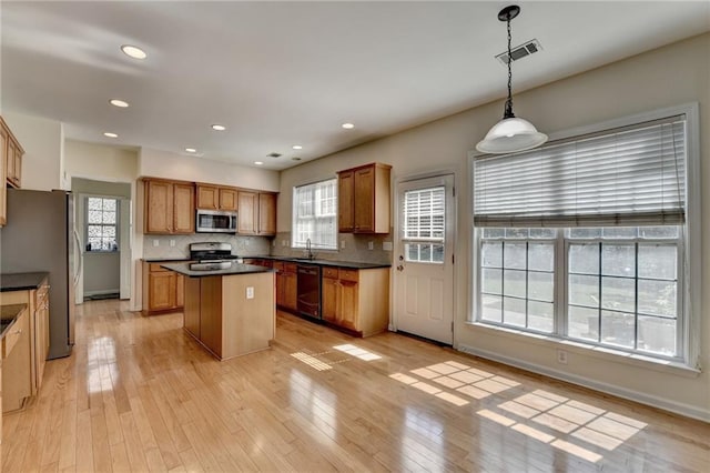 kitchen featuring stainless steel appliances, a kitchen island, dark countertops, backsplash, and light wood finished floors
