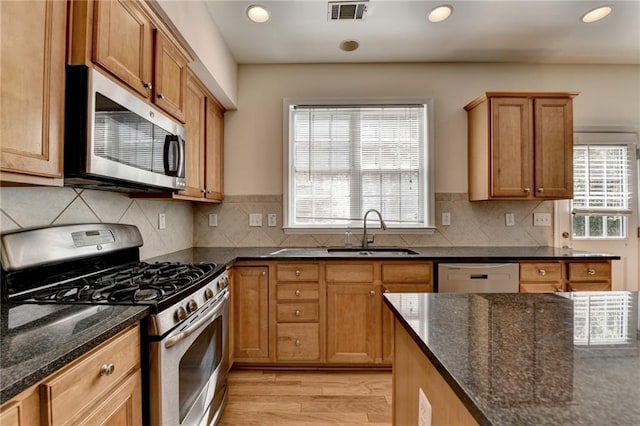 kitchen with stainless steel appliances, a sink, light wood-style flooring, dark stone countertops, and recessed lighting
