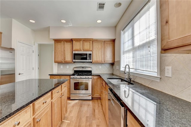kitchen featuring stainless steel appliances, light wood-style flooring, a sink, dark stone counters, and tasteful backsplash