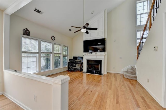 living area featuring high vaulted ceiling, a ceiling fan, light wood finished floors, stairway, and a fireplace
