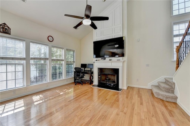 living room featuring high vaulted ceiling, ceiling fan, stairs, light wood finished floors, and baseboards