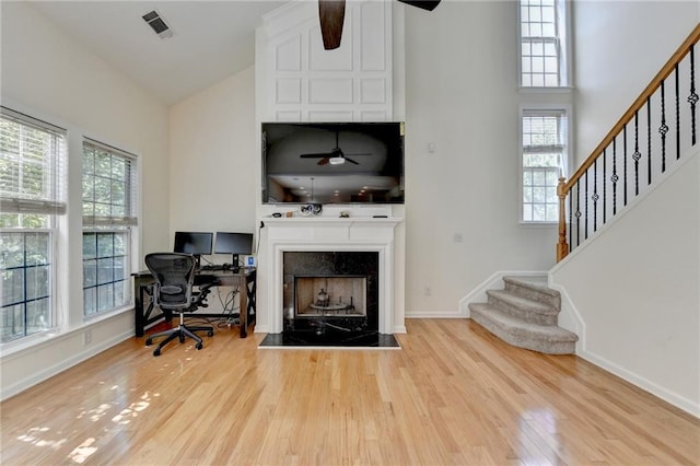 home office with ceiling fan, high vaulted ceiling, wood finished floors, baseboards, and a fireplace with raised hearth