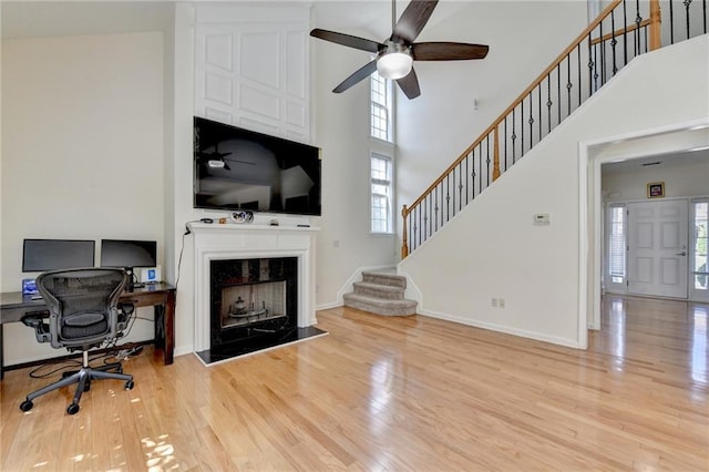 office area with a fireplace, plenty of natural light, wood finished floors, and a towering ceiling