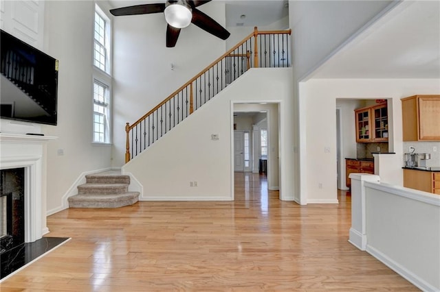unfurnished living room with a high ceiling, a ceiling fan, a high end fireplace, stairway, and light wood finished floors