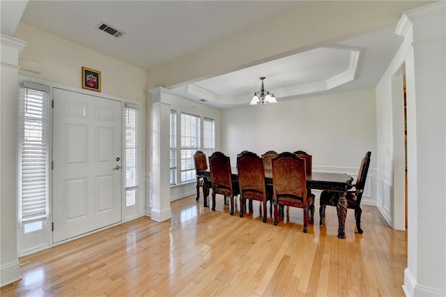 dining room with decorative columns, a chandelier, light wood-type flooring, and a tray ceiling