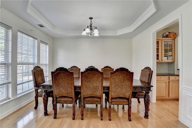dining space featuring healthy amount of natural light, a chandelier, a tray ceiling, light wood-style flooring, and crown molding
