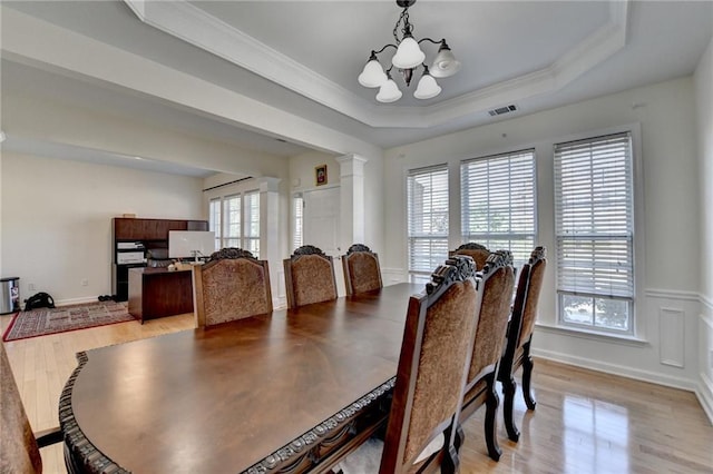 dining area with a chandelier, crown molding, light wood-type flooring, decorative columns, and a raised ceiling