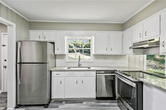 kitchen featuring appliances with stainless steel finishes, white cabinets, sink, hardwood / wood-style flooring, and light stone counters