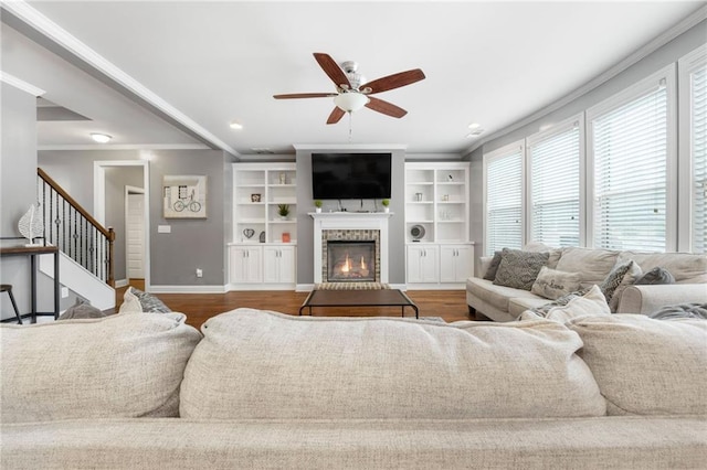 living room featuring wood finished floors, baseboards, a fireplace, ornamental molding, and stairs